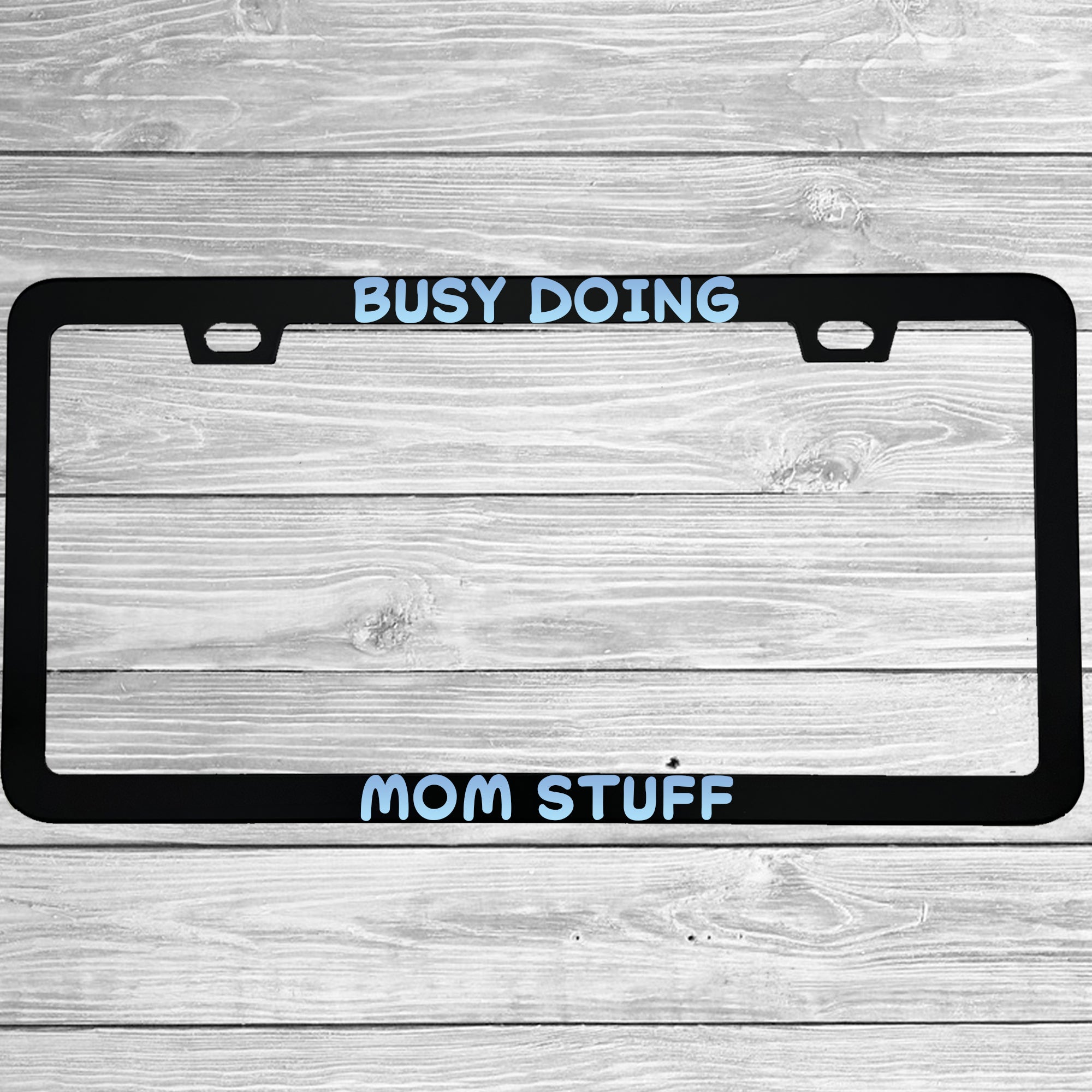 Close-up of "Busy Doing Mom Stuff" license plate frame showing fade-proof print quality