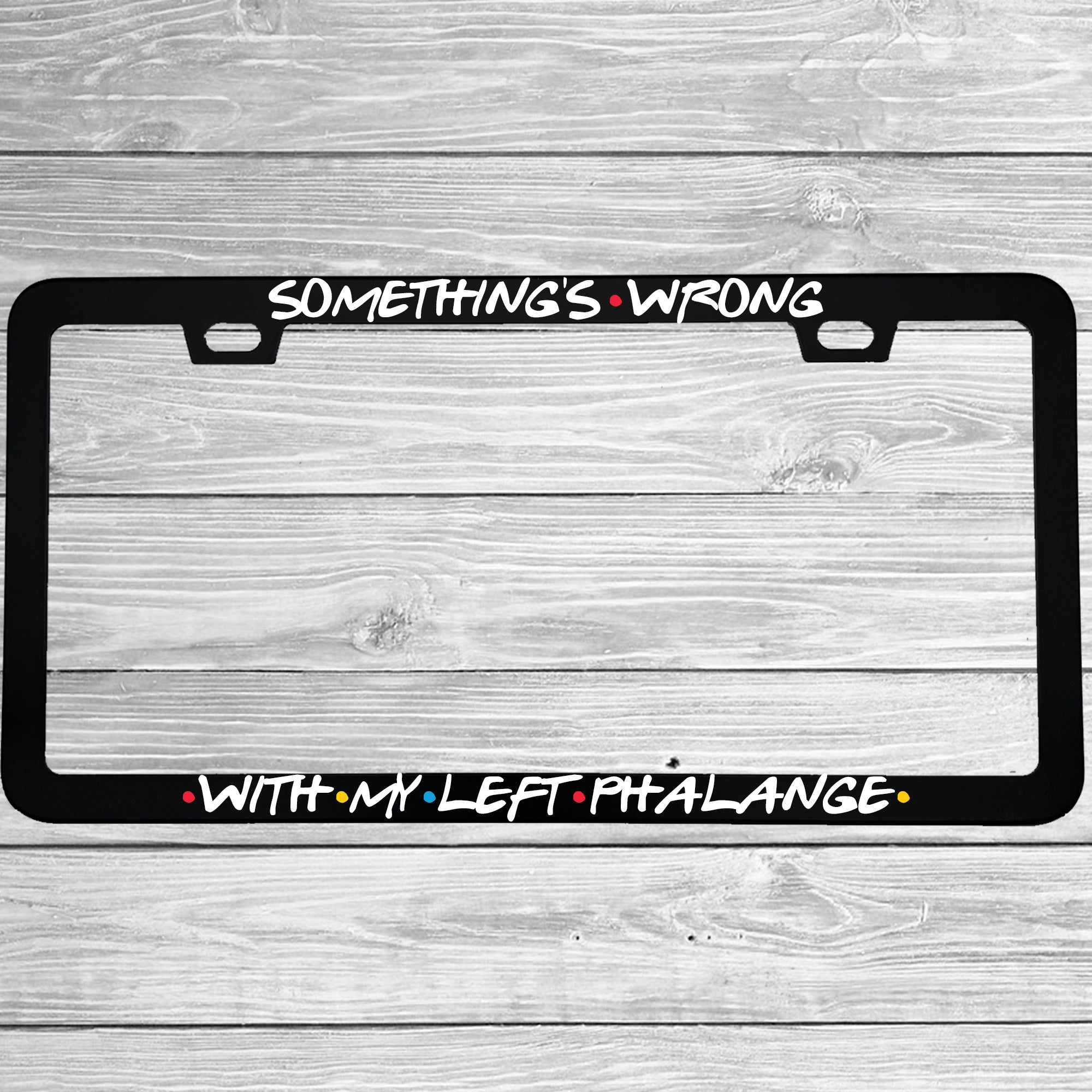 Close-up of "Something's Wrong With My Left Phalange" license plate frame showing fade-proof print quality