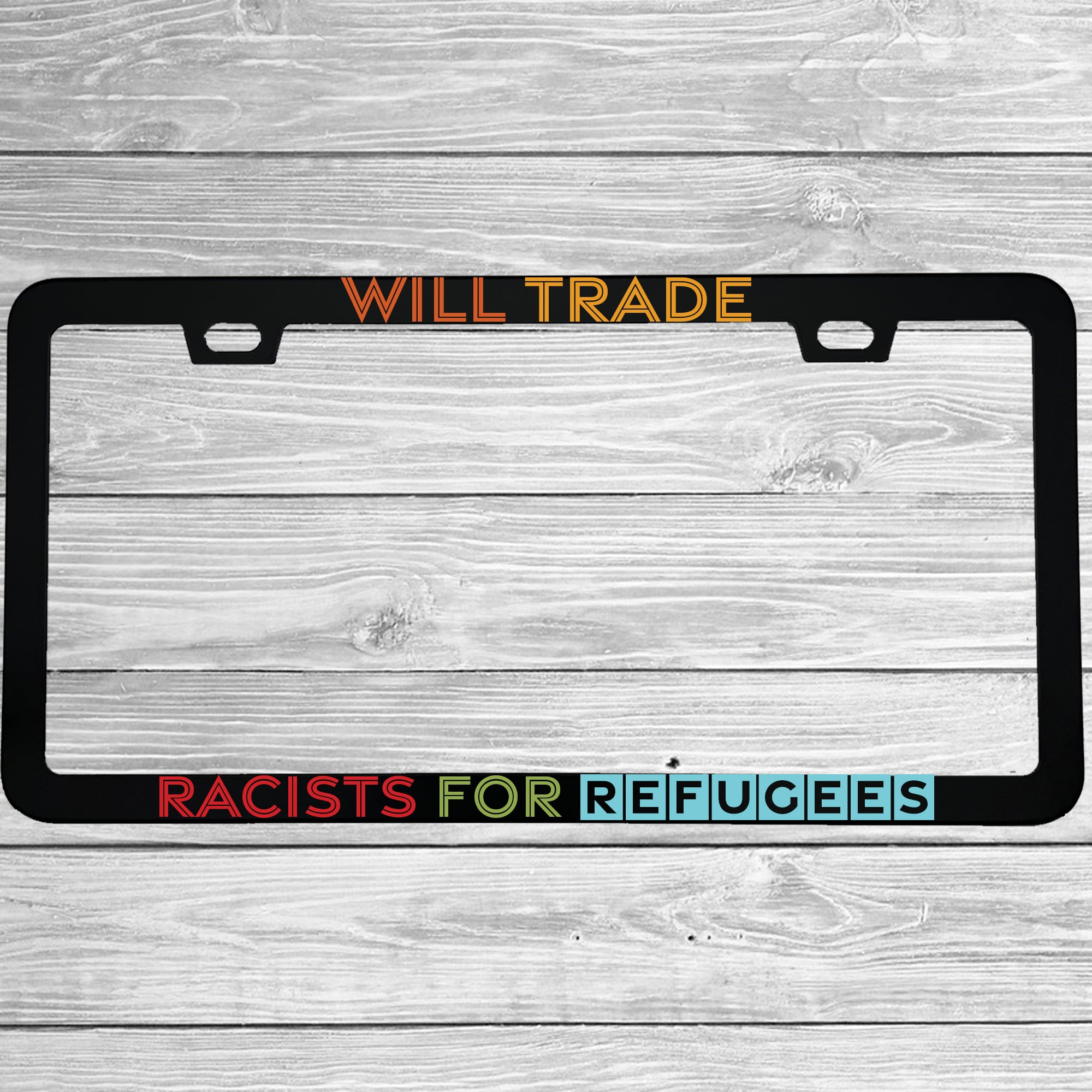 Close-up of "Will Trade Racists For Refugees" license plate frame showing fade-proof print quality