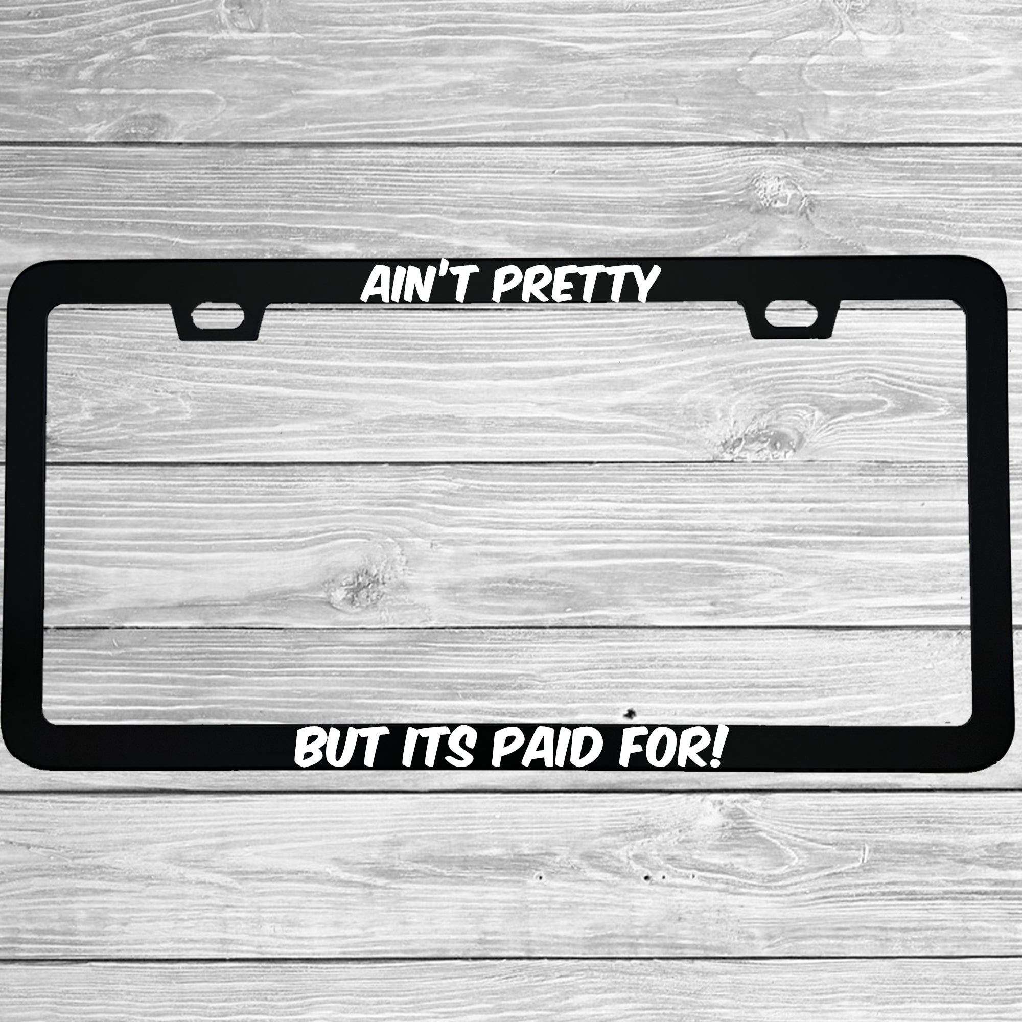 Close-up of "Ain't Pretty But Its Paid For" license plate frame showing fade-proof print quality
