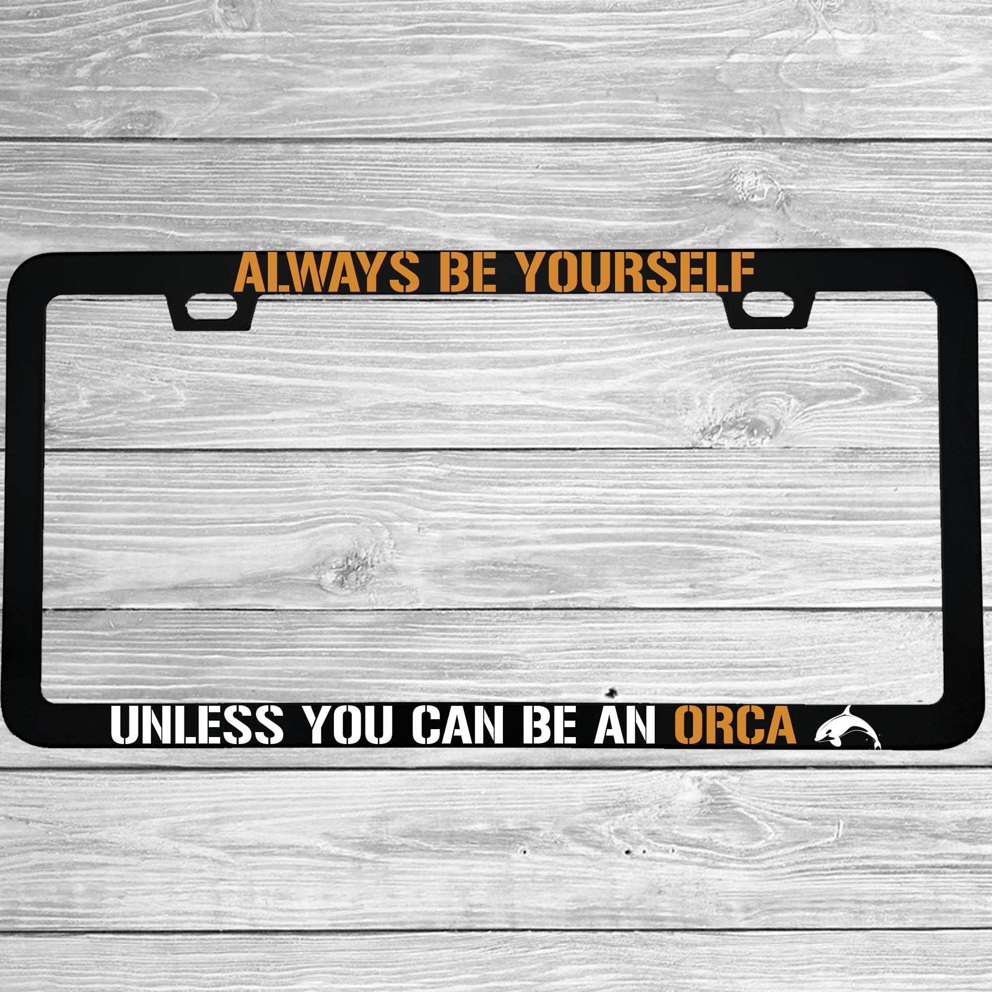 Close-up of "Always Be Yourself Unless You Can Be An Orca" license plate frame showing fade-proof print quality