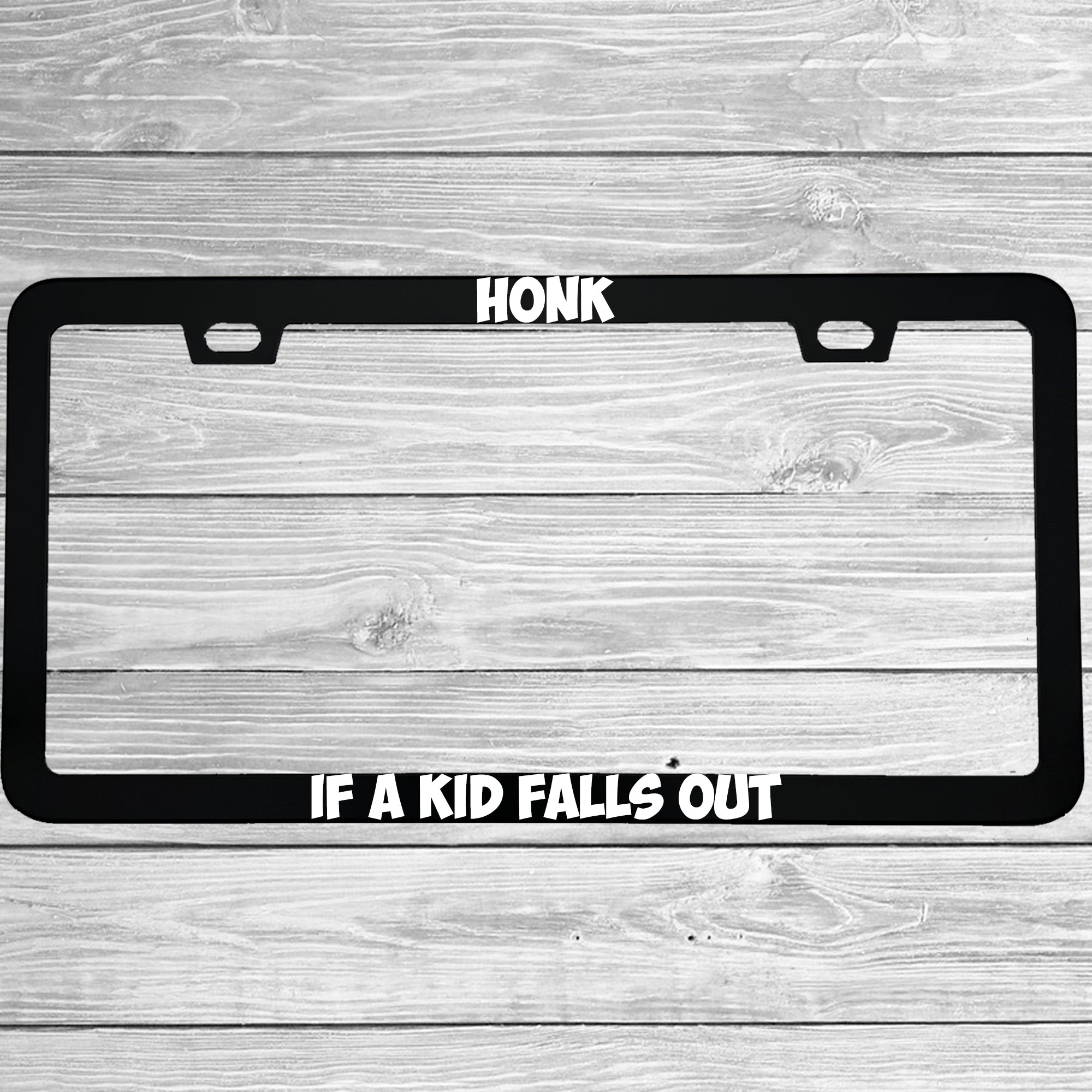 Close-up of "Honk If A Kid Falls Out" license plate frame showing fade-proof print quality