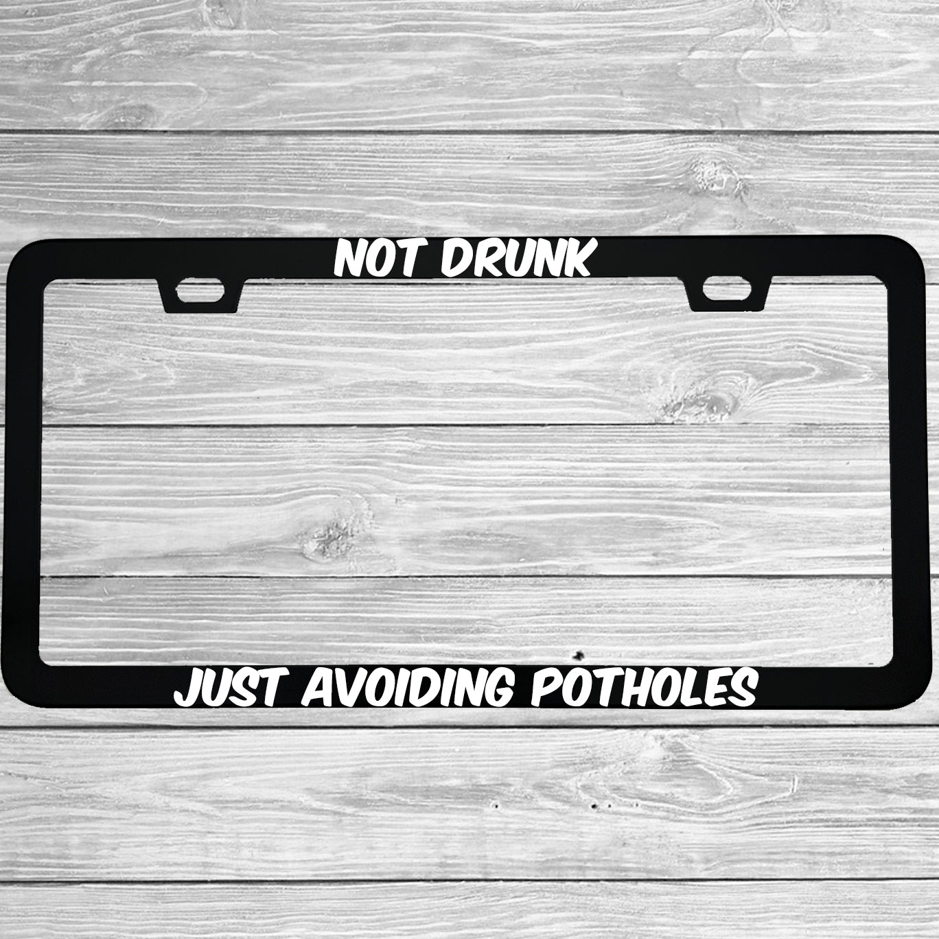 Close-up of "Not Drunk Just Avoiding Potholes" license plate frame showing fade-proof print quality